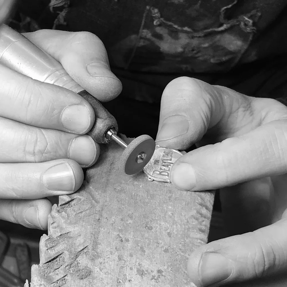 Hand finishing a Beatles drum logo necklace
